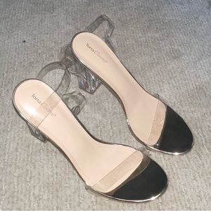 Nude clear high heel sandals with clear and gold straps .